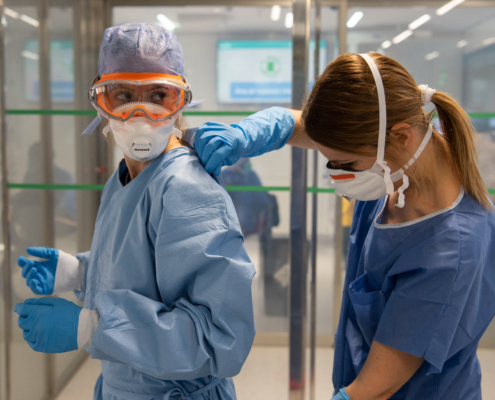 A healthcare worker helping another worker put on PPE