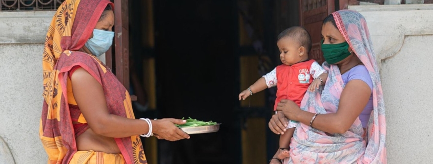 Two Indian woman and a baby. One woman is holding a plate of vegetables