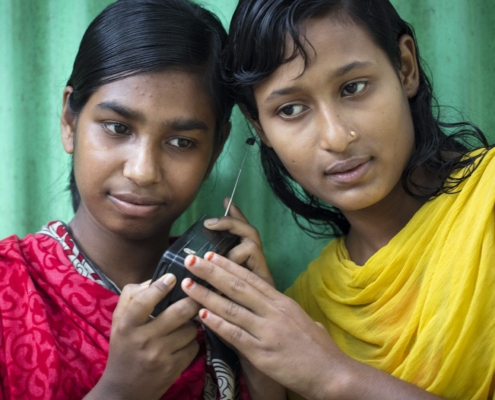 Two women listening to the radio. Photo credit: RCCE Collective Service