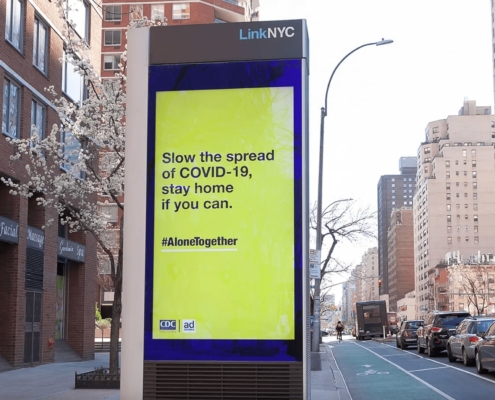 An electronic billboard in New York City that reads "Slow the spread of COVID-19, stay home if you can. #AloneTogether"