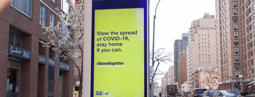 An electronic billboard in New York City that reads "Slow the spread of COVID-19, stay home if you can. #AloneTogether"