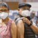 Two people wearing masks and showing where they received a COVID-19 vaccine.