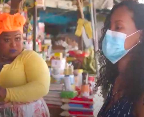 Two women in a market and one is wearing a mask.